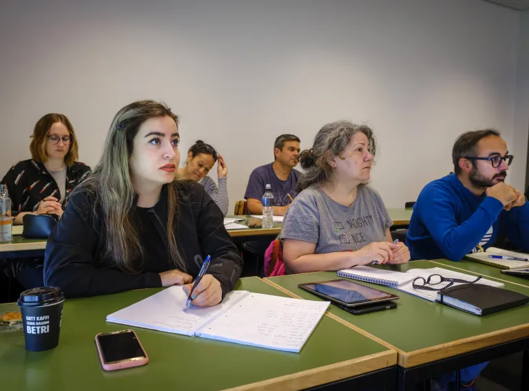 Nemendur sitja við borð í kennslustofu og hlusta á fyrirlestur.