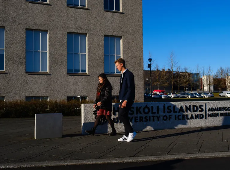 Tveir nemendur á gangi fyrir framan aðalbyggingu HÍ